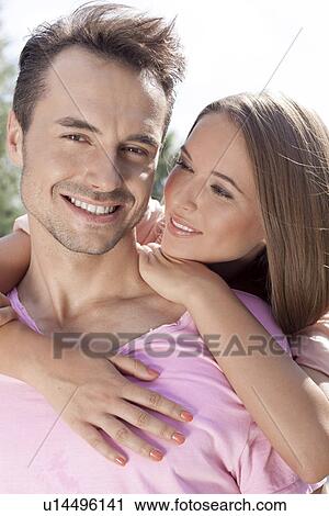 Beautiful young woman embracing man from behind in park View Large Photo Image Stock Image - Beautiful young woman embracing man from behind in park. Fotosearch