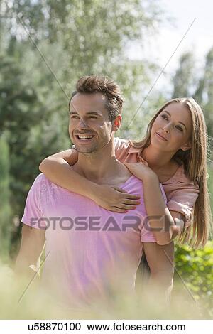 Stock Image - Beautiful young woman embracing man from behind in park. Fotosearch