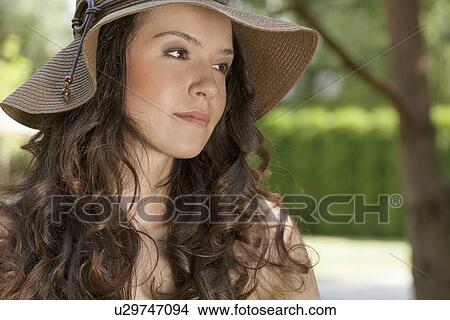 Picture - Beautiful young woman in sunhat looking away in park. Fotosearch