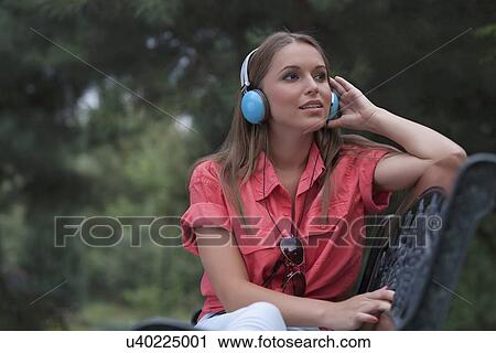 Stock Image - Beautiful young woman listening musing through headphones in park. Fotosearch