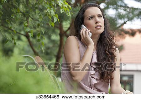 Stock Photography - Beautiful young woman looking away while on call at park. Fotosearch