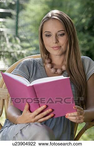 Stock Image - Beautiful young woman reading book in park. Fotosearch