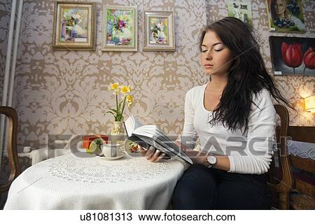 Stock Image - Beautiful young woman reading book in cafe. Fotosearch