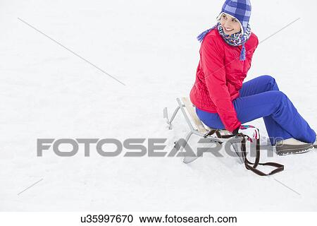 Stock Image - Beautiful young woman sitting on sled. Fotosearch