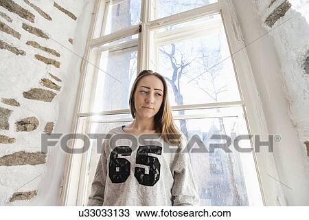 Beautiful young woman standing against window at home View Large Photo Image Stock Image - Beautiful young woman standing against window at home. Fotosearch