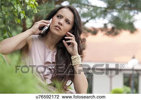 Beautiful young woman using cell phone in park View Large Photo Image Stock Image - Beautiful young woman using cell phone in park. Fotosearch