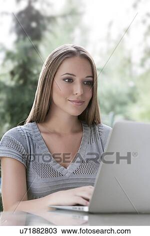 Stock Image - Beautiful young woman using laptop in park. Fotosearch