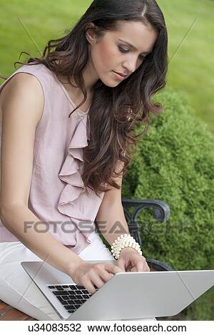 Beautiful young woman using laptop on bench in park View Large Photo Image Stock Image - Beautiful young woman using laptop on bench in park. Fotosearch