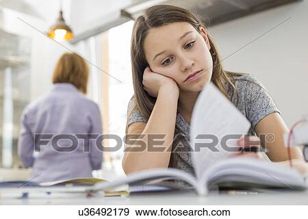 Stock Photo - Bored girl studying at table with mother standing in background. Fotosearch