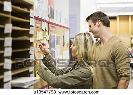 Stock Photo - Business people reading reminders on bulletin board in office. Fotosearch