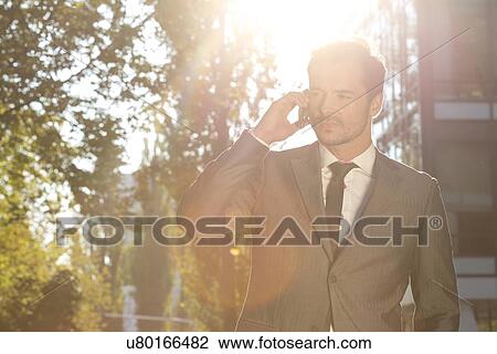 Stock Image - Businessman using cell phone outdoors. Fotosearch