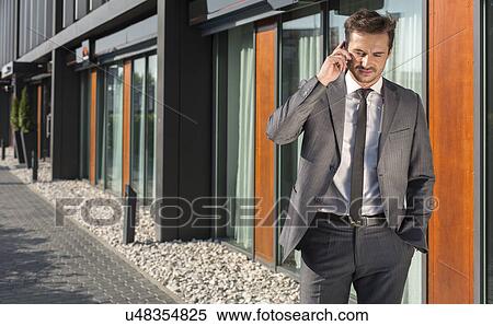 Stock Photography - Businessman using cell phone outside office. Fotosearch