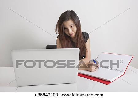 Businesswoman writing in diary while looking at laptop in office View Large Photo Image Stock Image - Businesswoman writing in diary while looking at laptop in office. Fotosearch