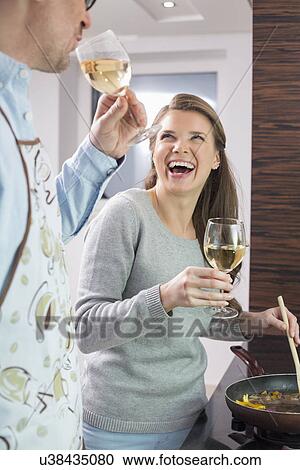 Stock Image - Cheerful couple having wine while cooking in kitchen. Fotosearch
