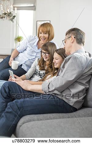 Stock Photo - Cheerful family using tablet PC on sofa at home. Fotosearch