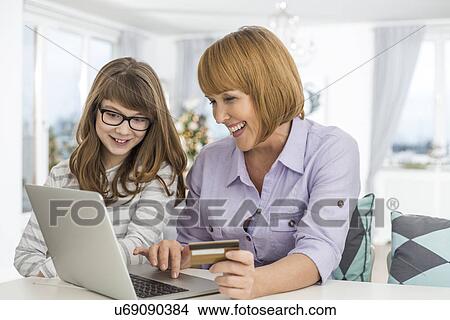 Picture - Cheerful mother and daughter shopping online at home during Christmas. Fotosearch
