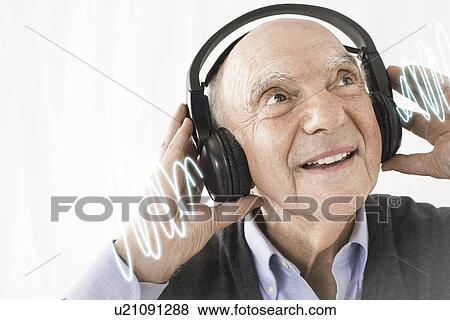 Cheerful senior man listening music through headphones against white background View Large Photo Image Stock Photo - Cheerful senior man listening music through headphones against white background. Fotosearch