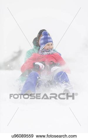 Stock Photo - Cheerful young couple sledding in snow. Fotosearch