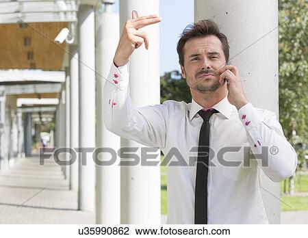 Stock Image - Confident young businessman gesturing while using mobile phone outside office. Fotosearch