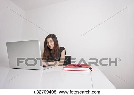 Confident young businesswoman using laptop at office desk View Large Photo Image Stock Photo - Confident young businesswoman using laptop at office desk. Fotosearch