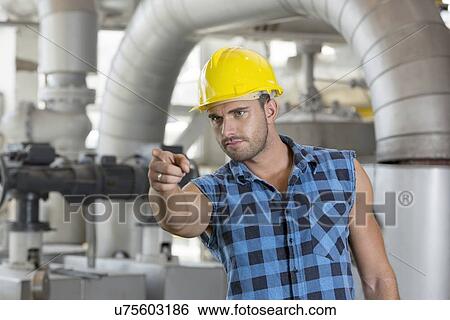 Confident young male worker pointing away in industry View Large Photo Image Stock Photograph - Confident young male worker pointing away in industry. Fotosearch