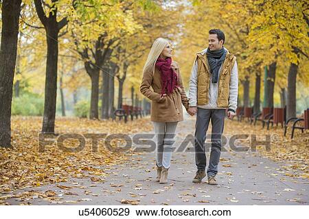 Couple holding hands while walking in park during autumn View Large Photo Image Stock Photo - Couple holding hands while walking in park during autumn. Fotosearch