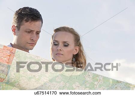 Stock Image - Couple reading map against sky. Fotosearch
