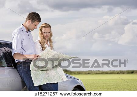 Couple reading map while leaning on car at countryside View Large Photo Image Stock Photo - Couple reading map while leaning on car at countryside. Fotosearch