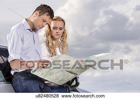 Couple reading map while leaning on car against cloudy sky View Large Photo Image Stock Photo - Couple reading map while leaning on car against cloudy sky. Fotosearch