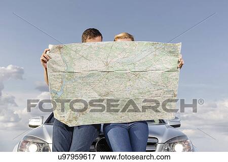 Couple reading map while leaning on car hood during road trip View Large Photo Image Stock Photo - Couple reading map while leaning on car hood during road trip. Fotosearch