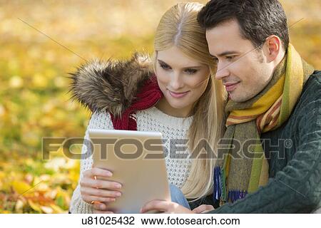 Couple using digital tablet in park during autumn View Large Photo Image Stock Image - Couple using digital tablet in park during autumn. Fotosearch