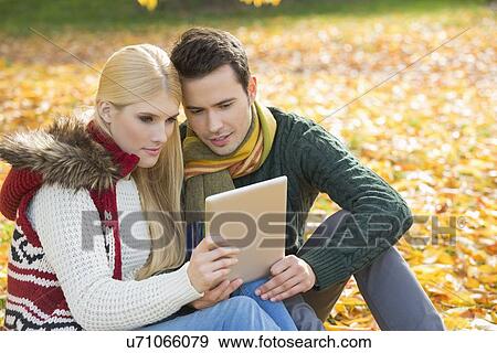 Couple using digital tablet together in park during autumn View Large Photo Image Stock Photo - Couple using digital tablet together in park during autumn. Fotosearch