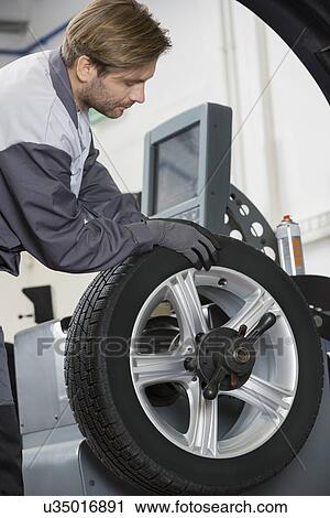 Stock Image - Cropped image of automobile mechanic repairing car's wheel in workshop. Fotosearch