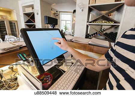 Stock Photo - Cropped image of cashier touching computer screen at restaurant counter. Fotosearch