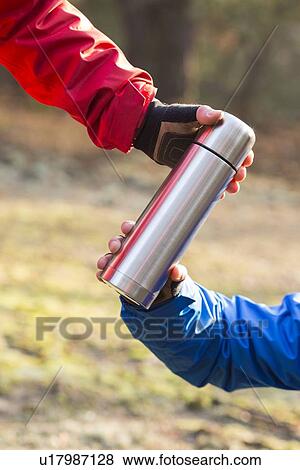 Stock Photo - Cropped image of hikers holding insulated coffee container in forest. Fotosearch