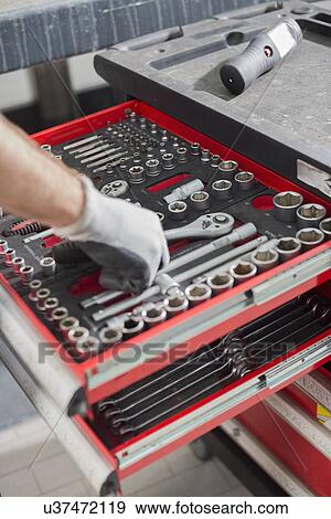 Stock Photo - Cropped image of male mechanic taking tool from drawer in car workshop. Fotosearch