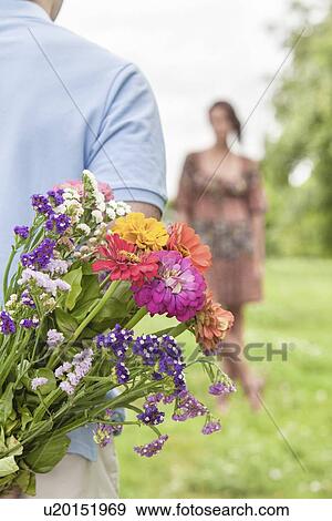 Cropped image of man hiding bouquet from woman in park View Large Photo Image Stock Photo - Cropped image of man hiding bouquet from woman in park. Fotosearch