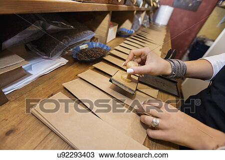 Stock Image - Cropped image of salesperson stamping paper bags at coffee store. Fotosearch