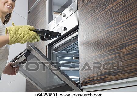 Stock Image - Cropped image of smiling woman removing dish from oven. Fotosearch