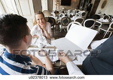Stock Image - Cropped image of waiter showing menu to couple in restaurant. Fotosearch