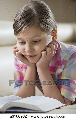 Picture - Cute girl reading book while lying at home. Fotosearch