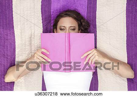 Stock Photo - Directly above shot of woman covering face with book while lying on striped picnic blanket. Fotosearch