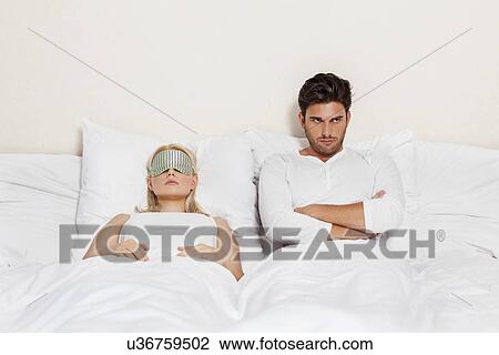 Stock Image - Displeased young man with woman sleeping in bed. Fotosearch