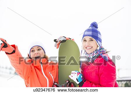 Stock Photograph - Excited female friends with snowboard outdoors. Fotosearch