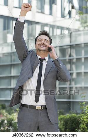 Excited young businessman using cell phone outside office View Large Photo Image Stock Image - Excited young businessman using cell phone outside office. Fotosearch