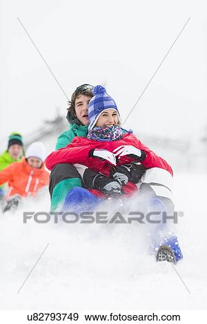 Stock Photo - Excited young friends sledding in snow. Fotosearch