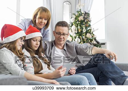 Stock Photo - Family of four using digital tablet at home during Christmas. Fotosearch