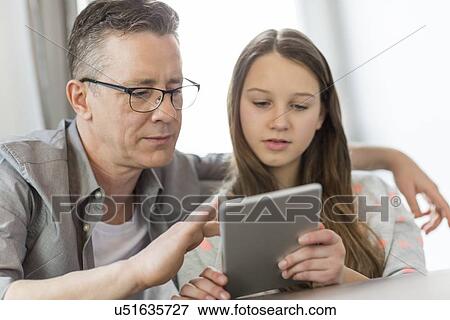 Stock Photo - Father and daughter using digital tablet at home. Fotosearch