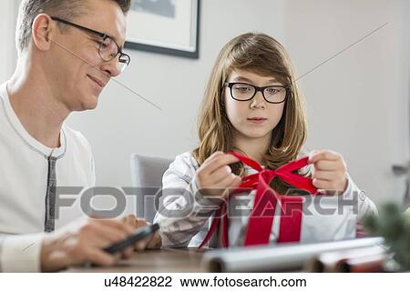 Stock Image - Father and daughter wrapping Christmas present at home. Fotosearch