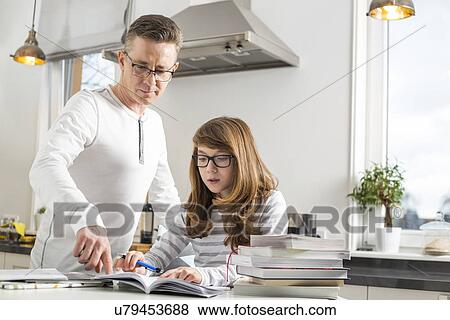 Stock Photo - Father guiding daughter in doing homework at table. Fotosearch